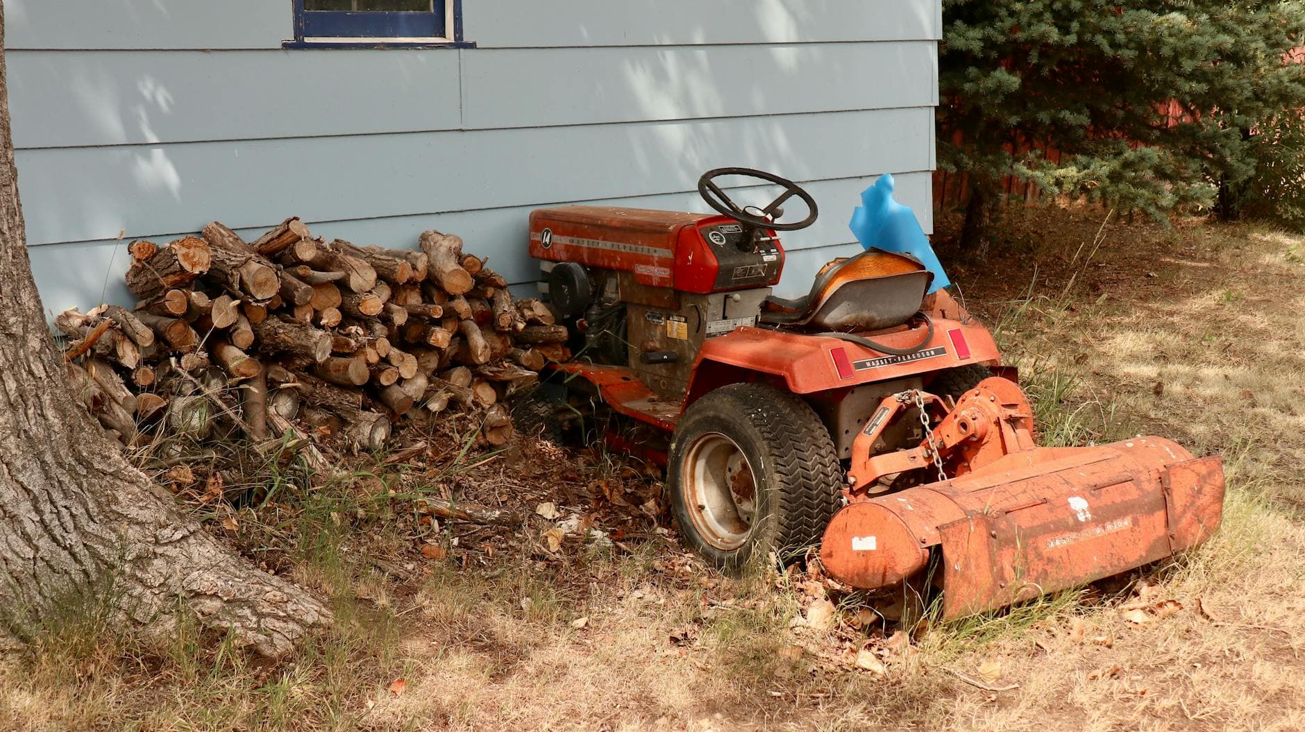An old red tractor beside a stack of firewood outdoors.