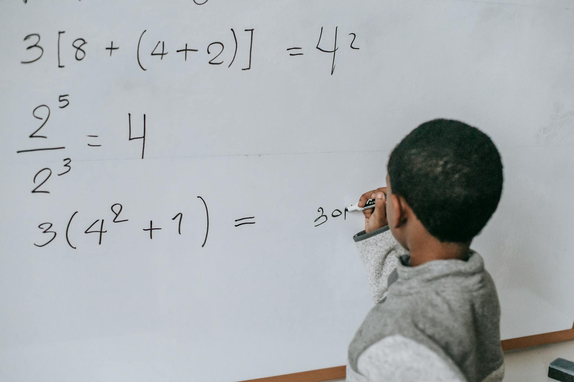 Back view of anonymous African American boy writing on whiteboard while doing sums on mathematics class