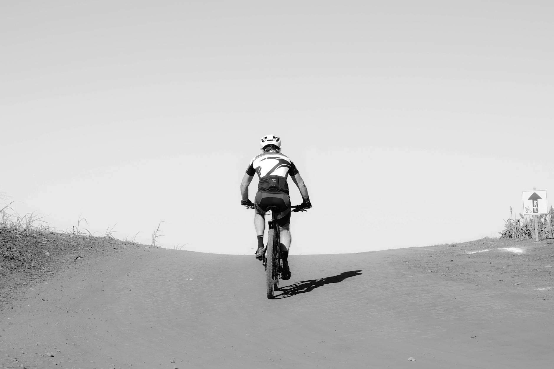 A cyclist ascends a dirt path on a sunny day, capturing the essence of outdoor adventure.