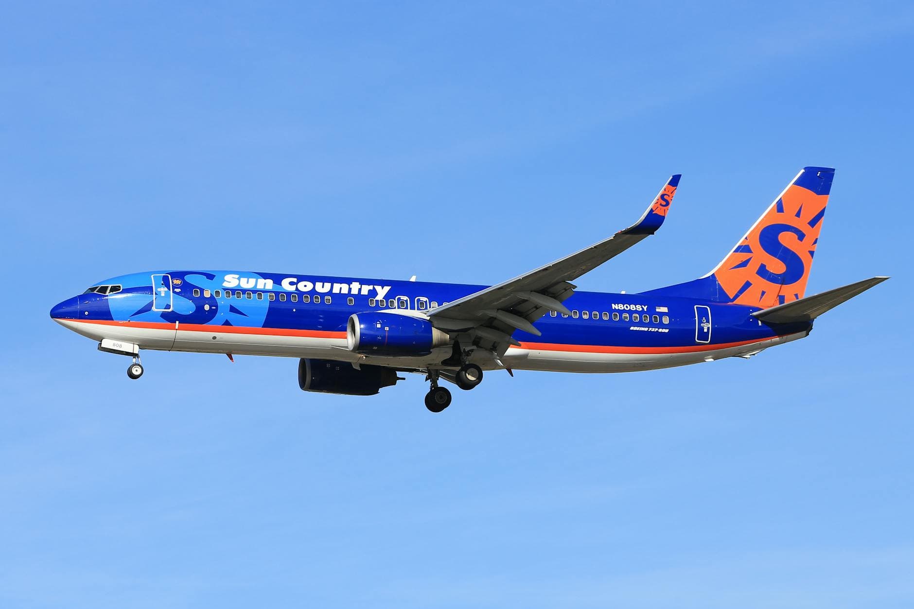 Boeing 737 from Sun Country Airlines soaring against a clear blue sky.