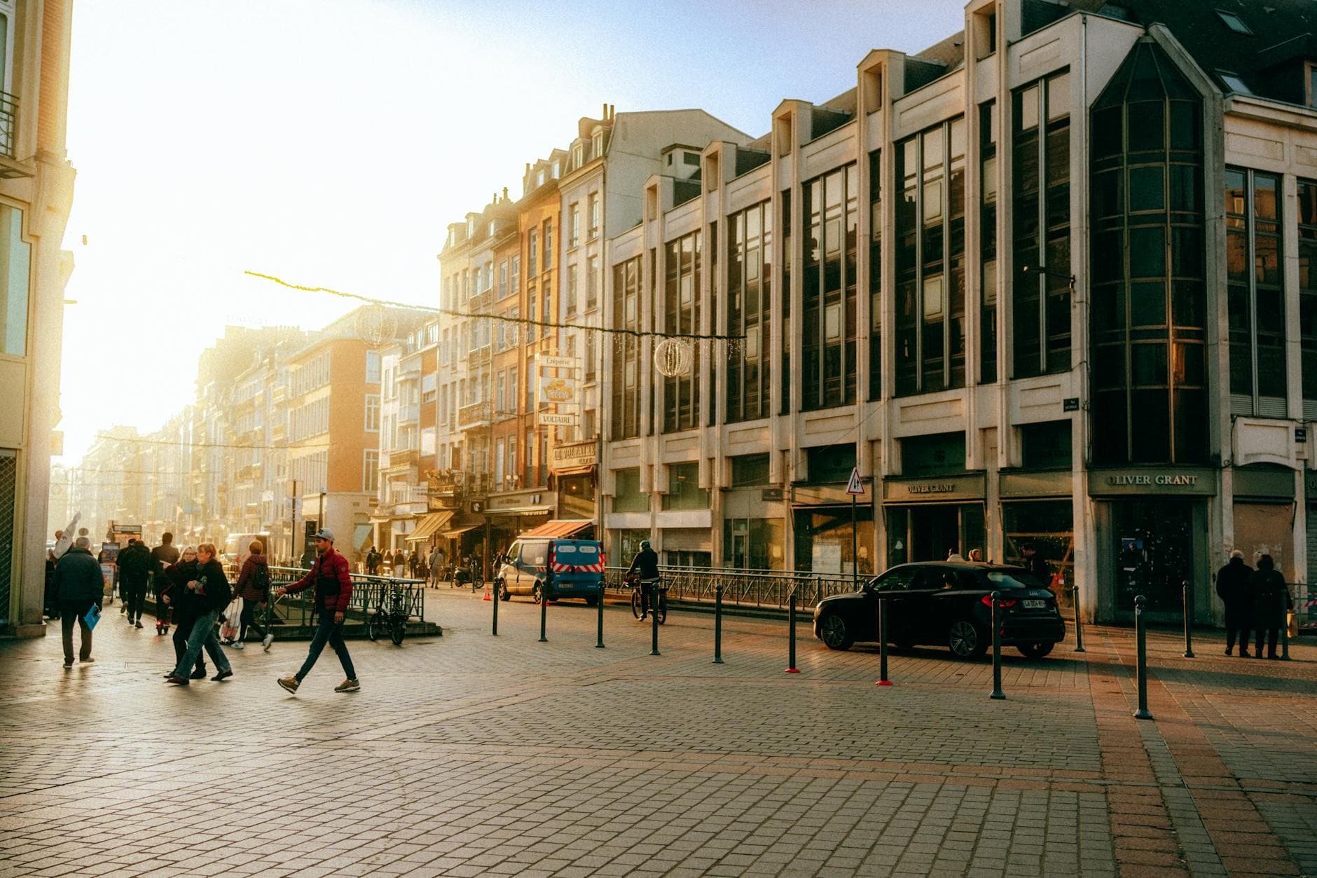 View of an urban street with people and cars during golden hour, creating a warm atmosphere.