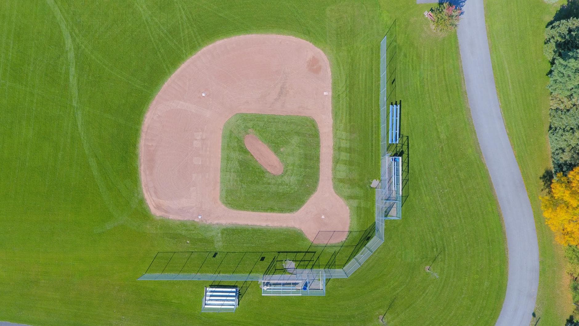 Aerial shot of a baseball field with green grass in a park setting, empty and serene.