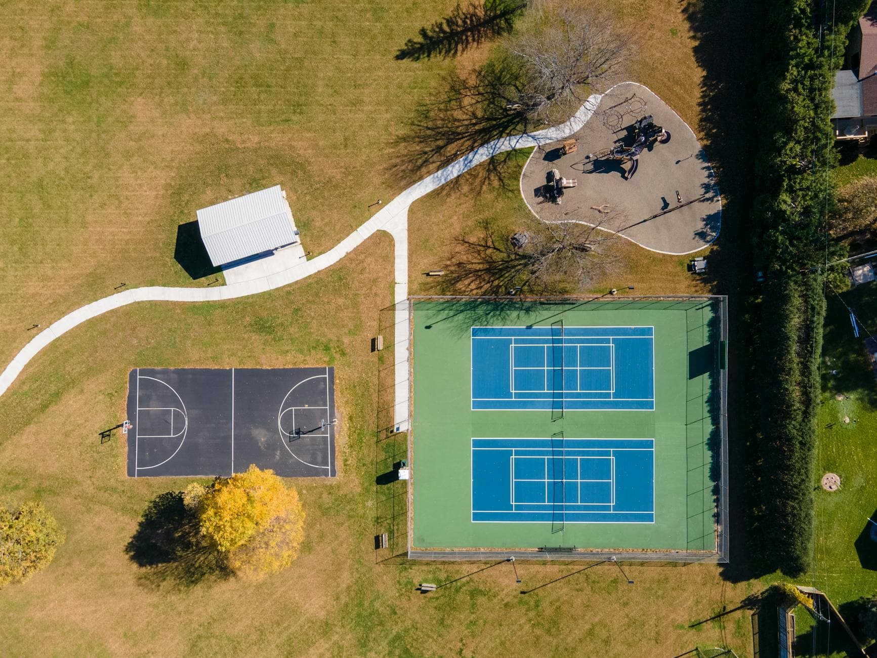 Drone shot showcasing tennis and basketball courts in a park setting, ideal for outdoor sports imagery.
