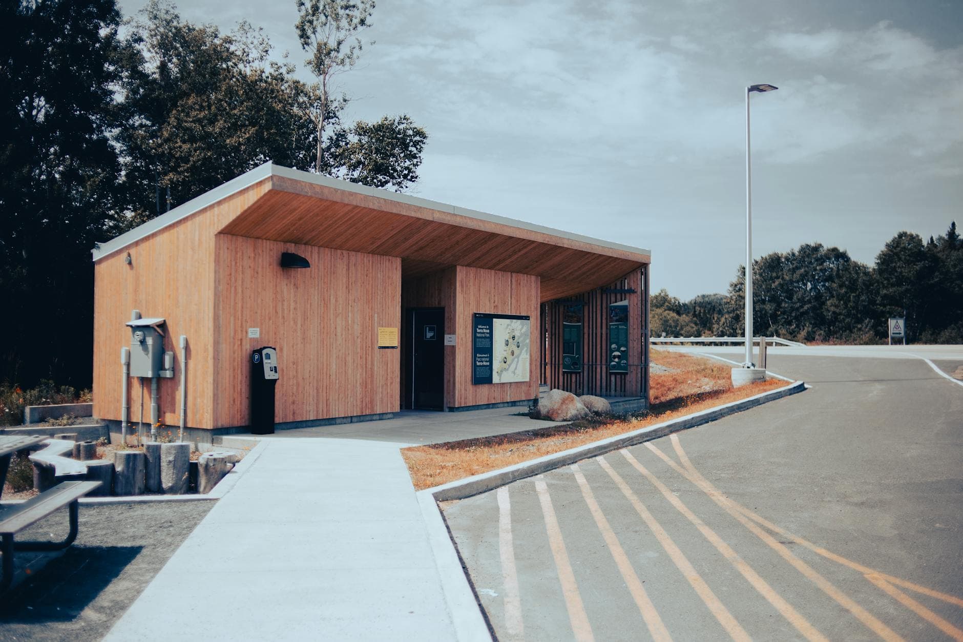 A wooden building at a roadside rest area with parking and a clear blue sky.