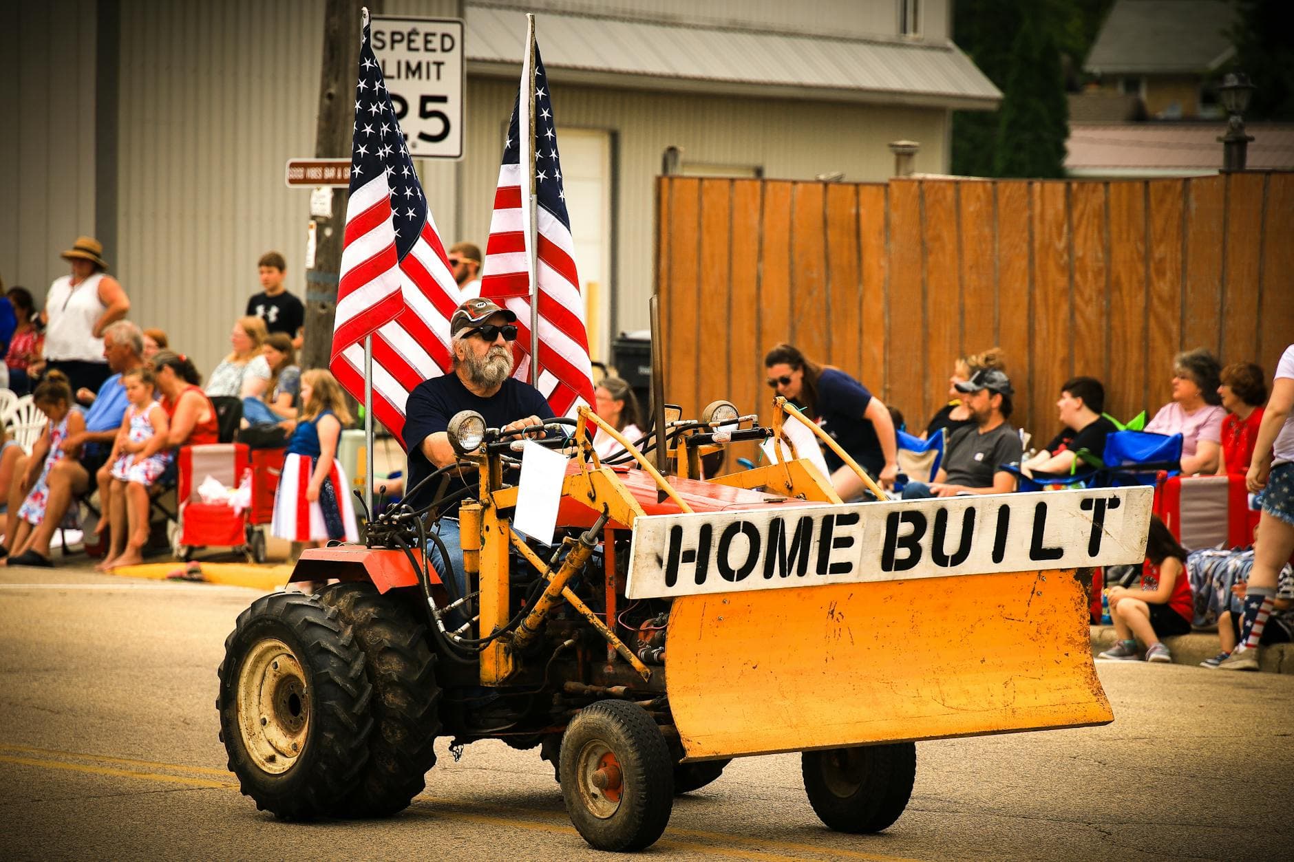 A community parade in Bonduel, WI featuring a man driving a homemade tractor adorned with American flags.