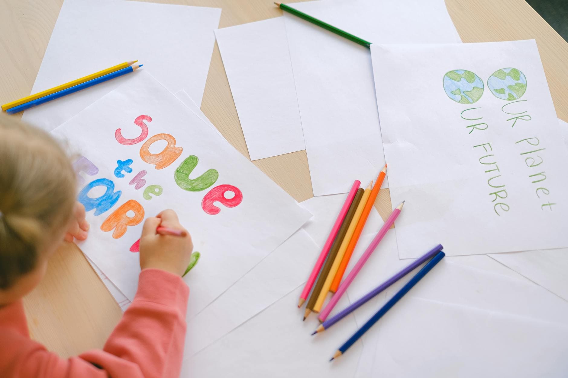 A child creatively illustrating a Save the Earth message using colored pencils for an educational project.