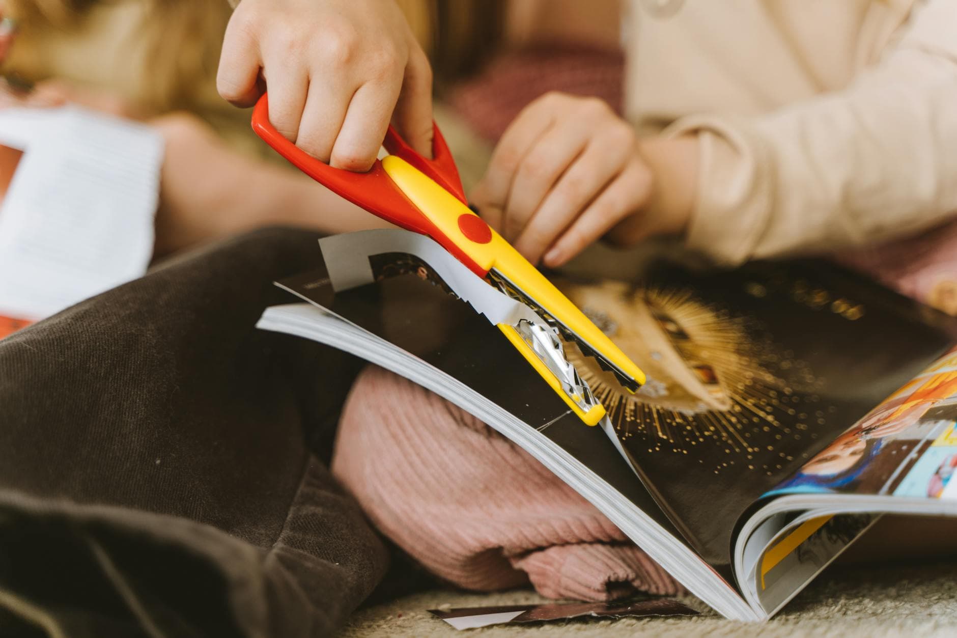 Close-up of a child using scissors to cut a magazine page for a craft project.