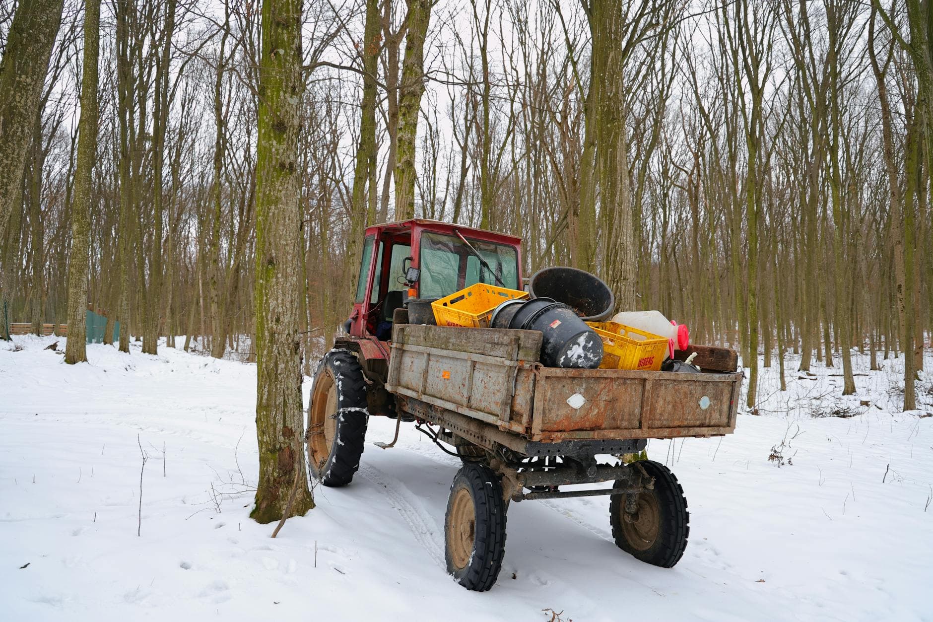A red tractor in a snowy forest carrying various cargo in its trailer.
