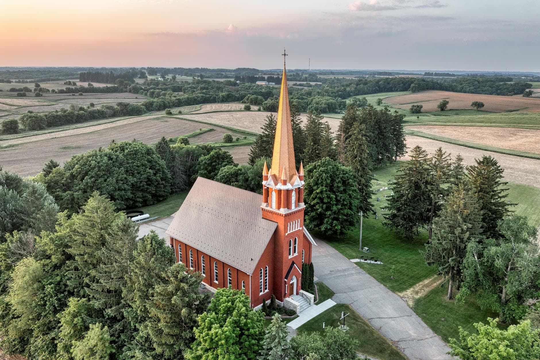 Drone view of a church surrounded by fields and trees in Lund, Wisconsin, during sunrise.