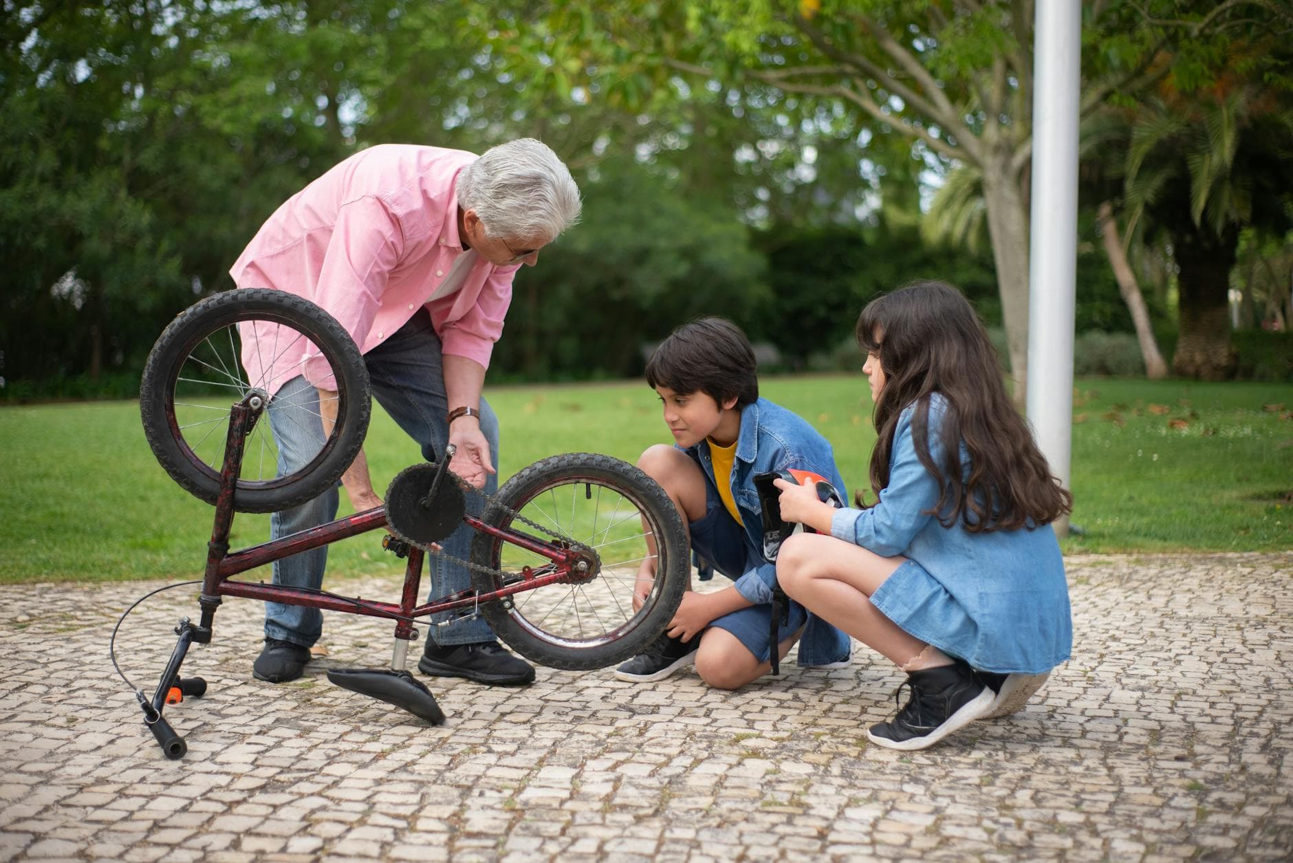 Grandfather and grandchildren repairing a bicycle together in a park, sharing a bonding experience outdoors.