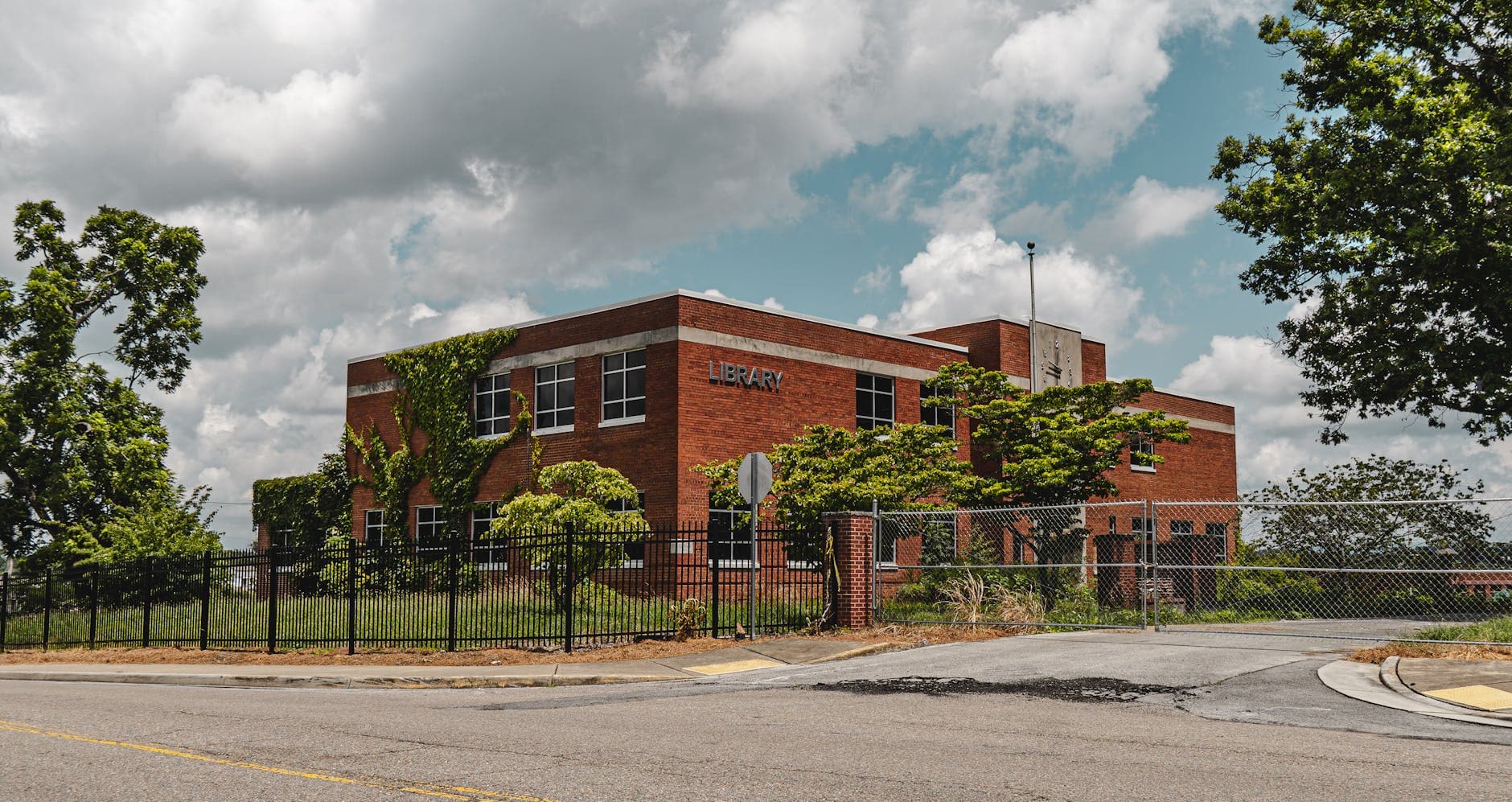 A deserted red brick library enveloped by nature, under a cloudy sky in Bristol, Virginia.