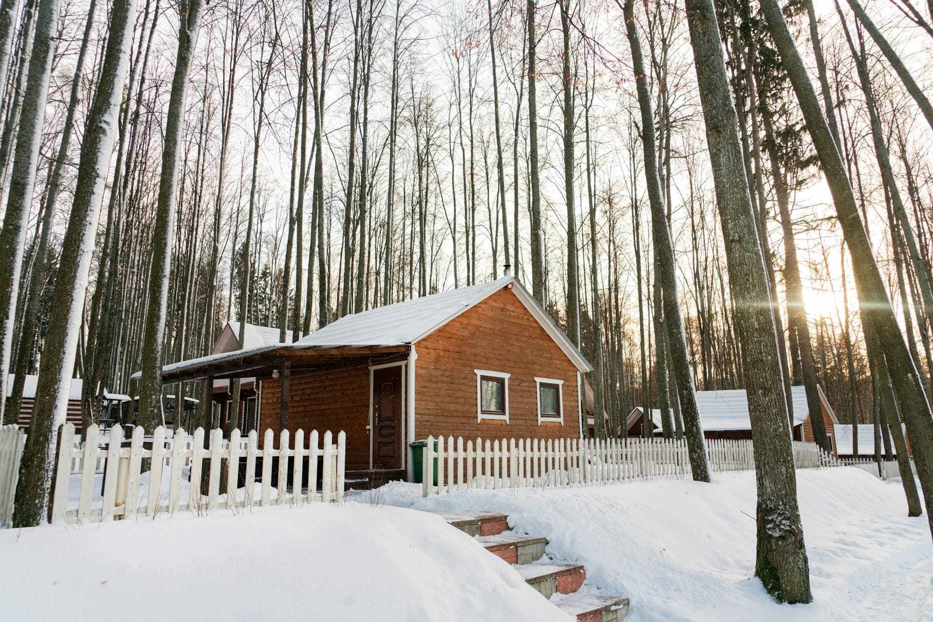 A serene winter scene of a cozy snow-covered cabin surrounded by bare trees.
