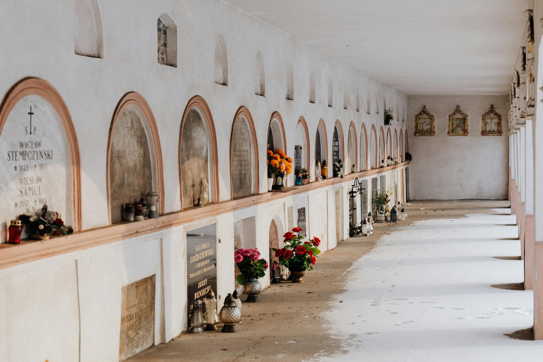 Quiet corridor in a cemetery with rows of tombs decorated with flowers and candles.