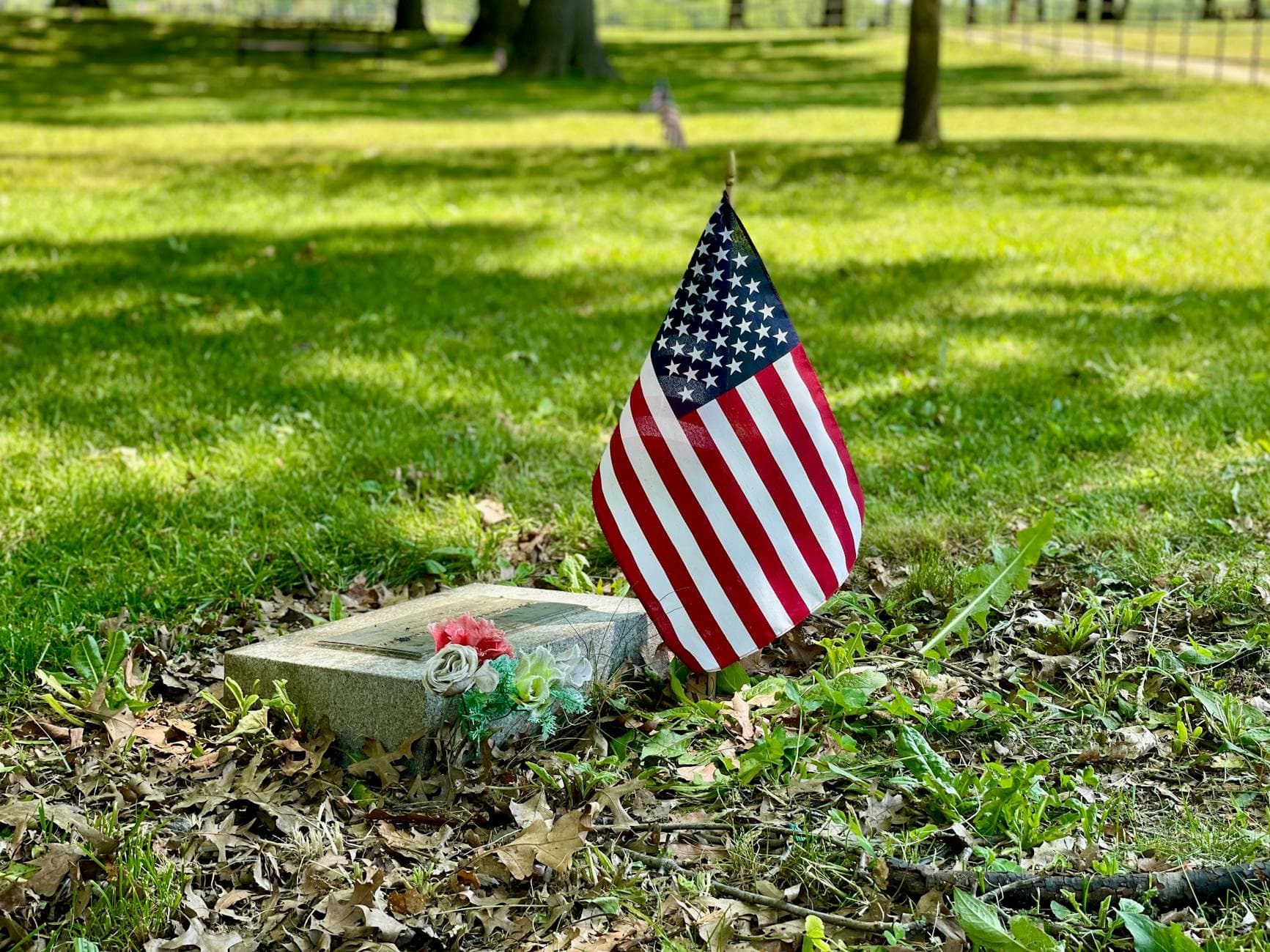 A solemn scene with an American flag beside a tombstone in a grassy cemetery.