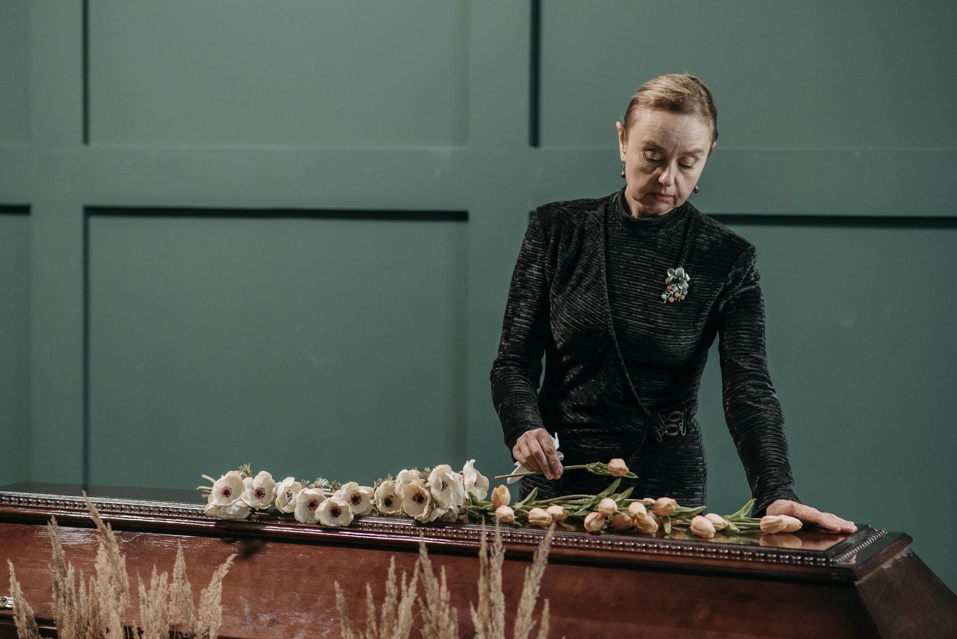 A solemn moment of a woman paying respects at a funeral, surrounded by flowers.