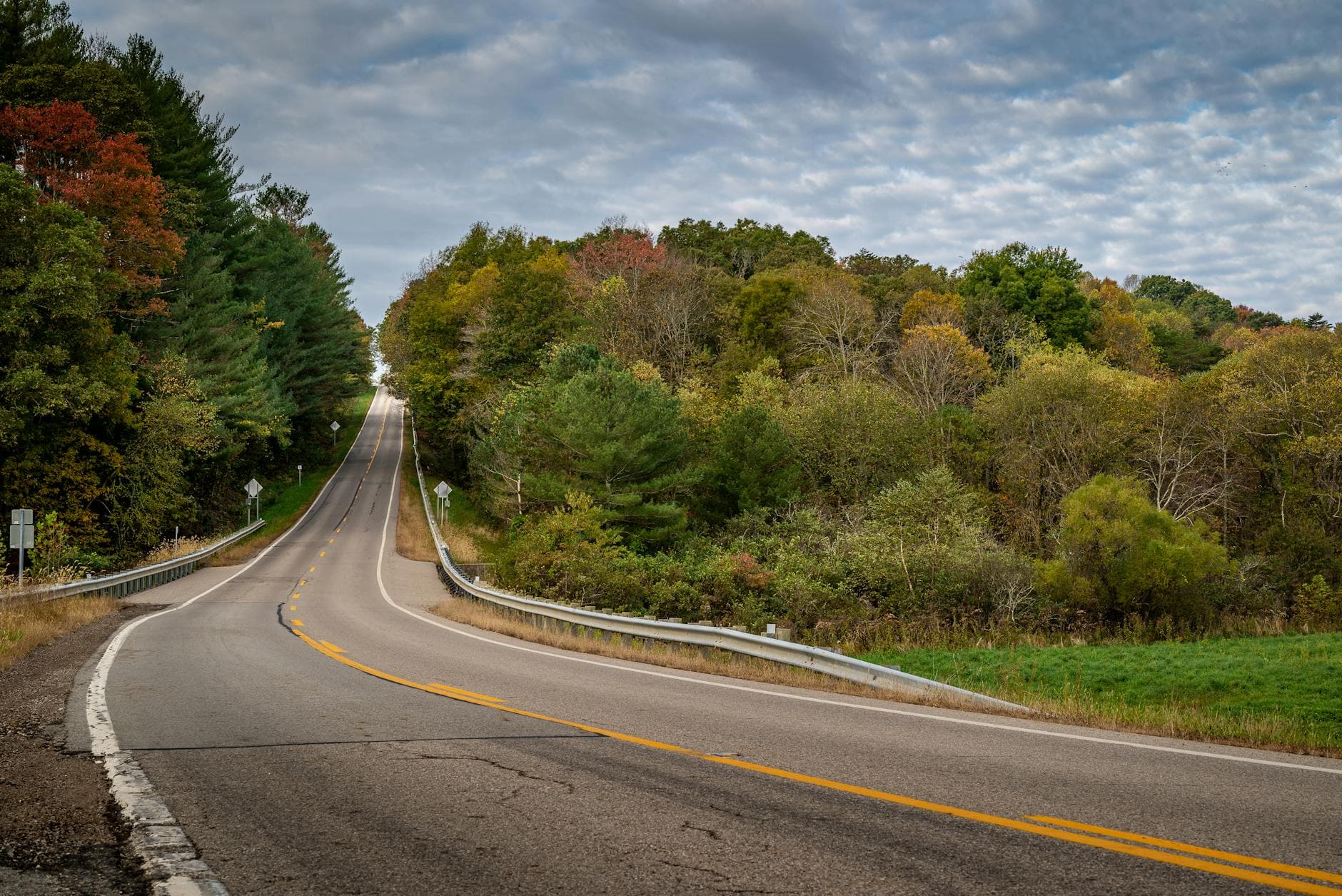Curving road through lush autumn foliage under a cloudy sky.
