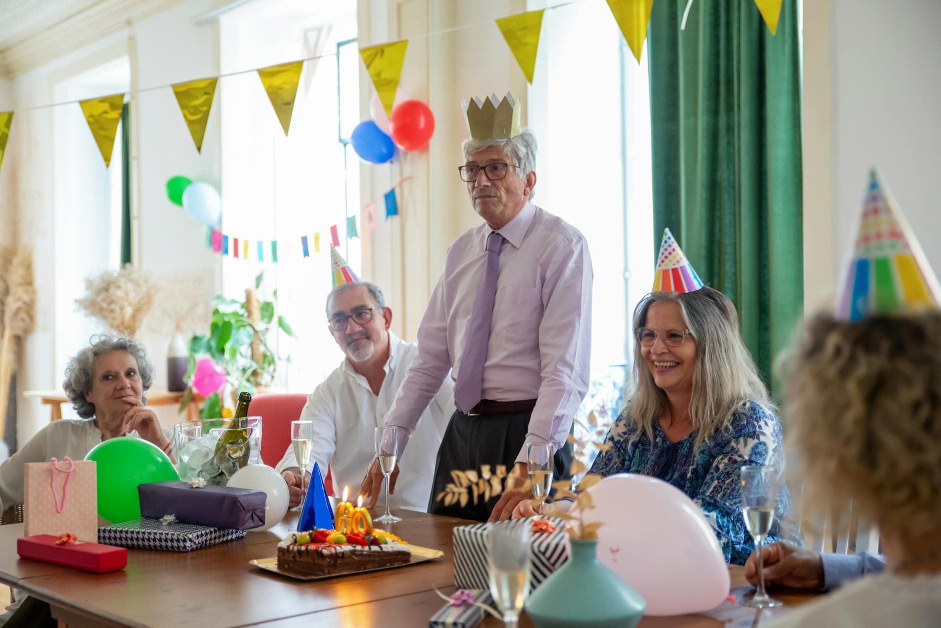 Smiling seniors celebrating a birthday party indoors with decorations and cake.