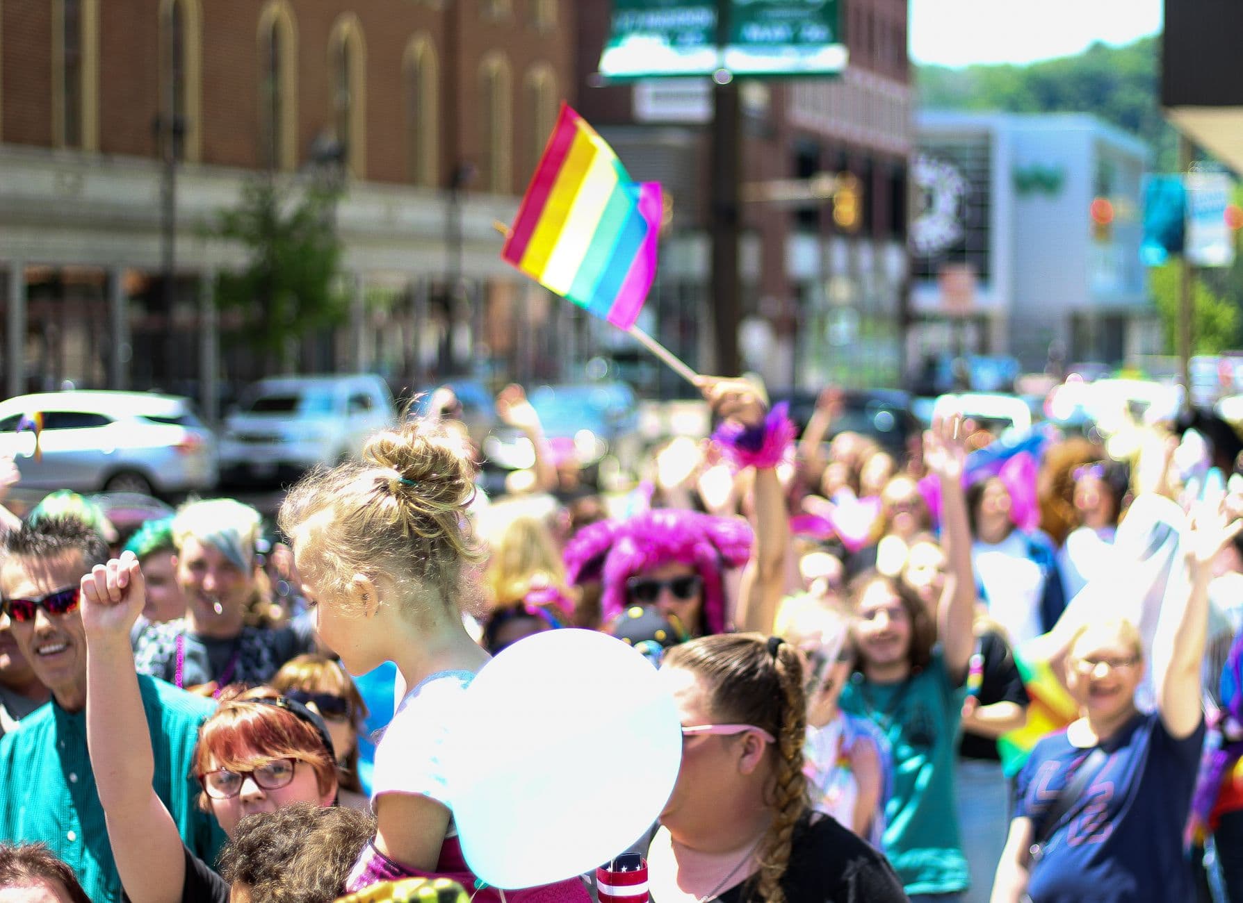 LGBTQ pride parade with multicolored flags and a lively crowd in a city street.
