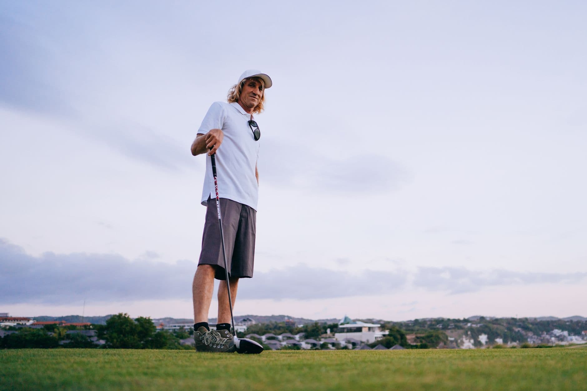 A man enjoying golf on a scenic course, under a clear sky, wearing relaxed attire.